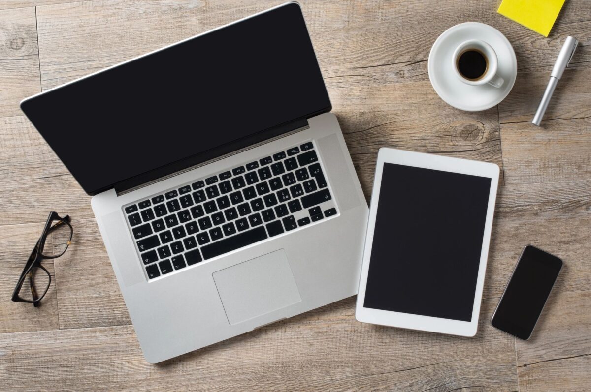 A laptop, electronic note pad, and a cellular phone on a desk.